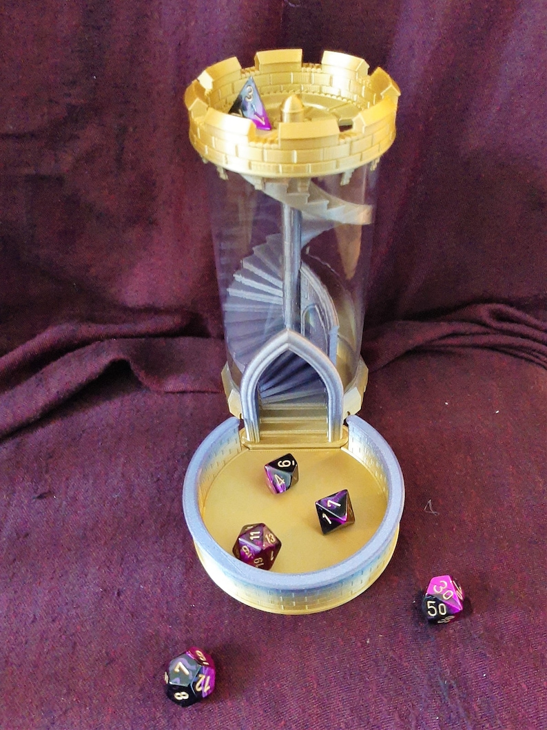 May include: A gold and silver tower-shaped dice rolling tower with a clear plastic tube and a spiral staircase inside. Four multi-colored dice with black and gold numbers are scattered around the tower.