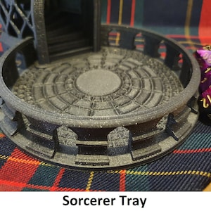 May include: A black 3D printed tray with a circular center and a raised outer edge. The tray has a textured surface and is designed to hold dice. The tray is sitting on a red and black plaid fabric.