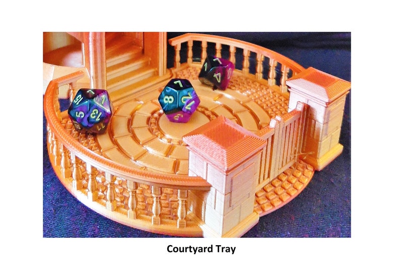 May include: A gold-colored 3D printed tray with a circular courtyard design. The tray has a gate and a balcony with railings. There are three iridescent dice on the tray, one blue, one purple, and one green.