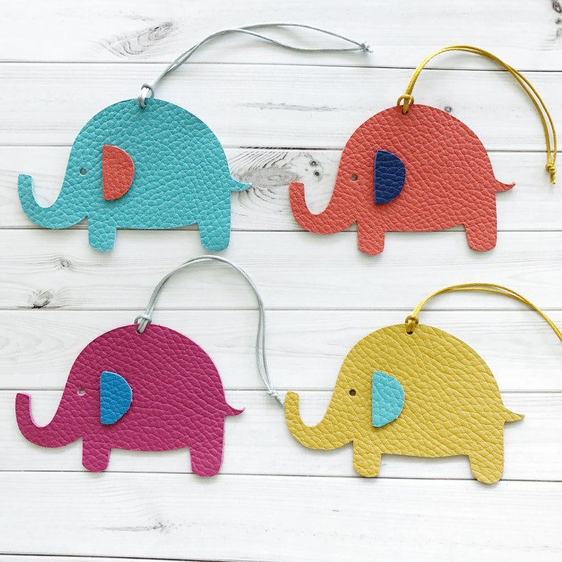 May include: Four leather elephant ornaments with different colored bodies and ears. The elephants are turquoise, coral, pink, and yellow. Each elephant has a blue eye.