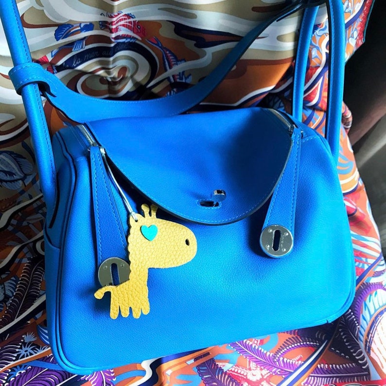 May include: A bright blue leather handbag with a flap closure and a small yellow giraffe charm. The bag has silver hardware and a top handle.