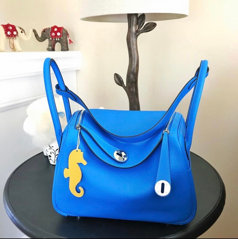 May include: A bright blue leather handbag with a silver clasp and a yellow seahorse charm. The bag has two top handles and a detachable shoulder strap.