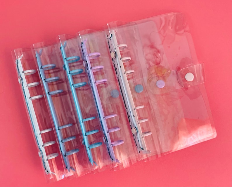 Op de afbeelding: Een set van zes transparante plastic binderhoezen met kleurrijke ringen. De hoezen zijn doorschijnend en laten een licht patroon zien. De ringen zijn in tinten blauw, paars en wit.