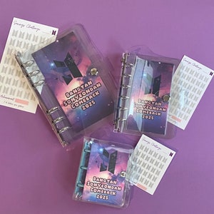 May include: Three clear plastic binders with a galaxy design and the text "BANGTAN SONYEONDAN COMEBACK 2025". Each binder has a silver ring mechanism and a clear plastic cover.