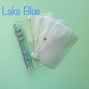 Op de afbeelding: Een transparante plastic map met meerdere transparante plastic ritsvakken. De map heeft een blauw ringmechanisme en de tekst "Lake Blue" staat in het blauw bovenaan de afbeelding.