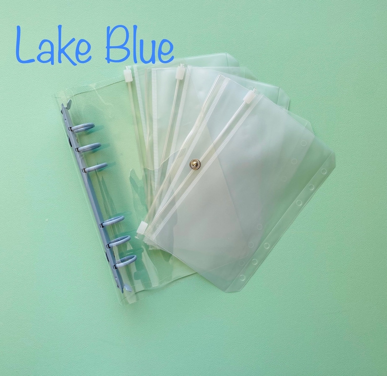 Op de afbeelding: Een transparante plastic map met meerdere transparante plastic ritsvakken. De map heeft een blauw ringmechanisme en de tekst "Lake Blue" staat in het blauw bovenaan de afbeelding.