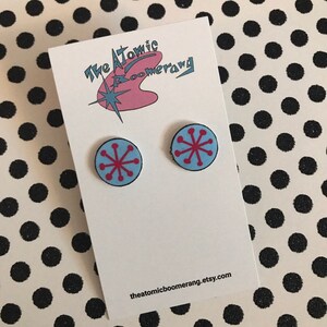 Peut inclure: Une paire de boucles d'oreilles clous bleues et roses avec un motif en forme d'étoile. Les boucles d'oreilles sont sur une carte blanche avec le texte "The Atomic Boomerang" et "theatomicboomerang.etsy.com".