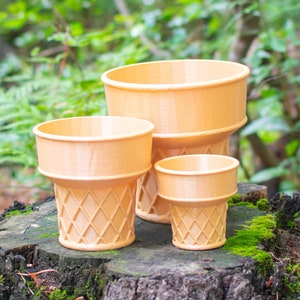 Three 3D printed ice cream cone planters arranged on a moss covered stump in a wooded area. They are made of a light brown plastic and are modeled to look like a cake cone. Each has a wide mouth and the bottom half has a waffle like pattern.