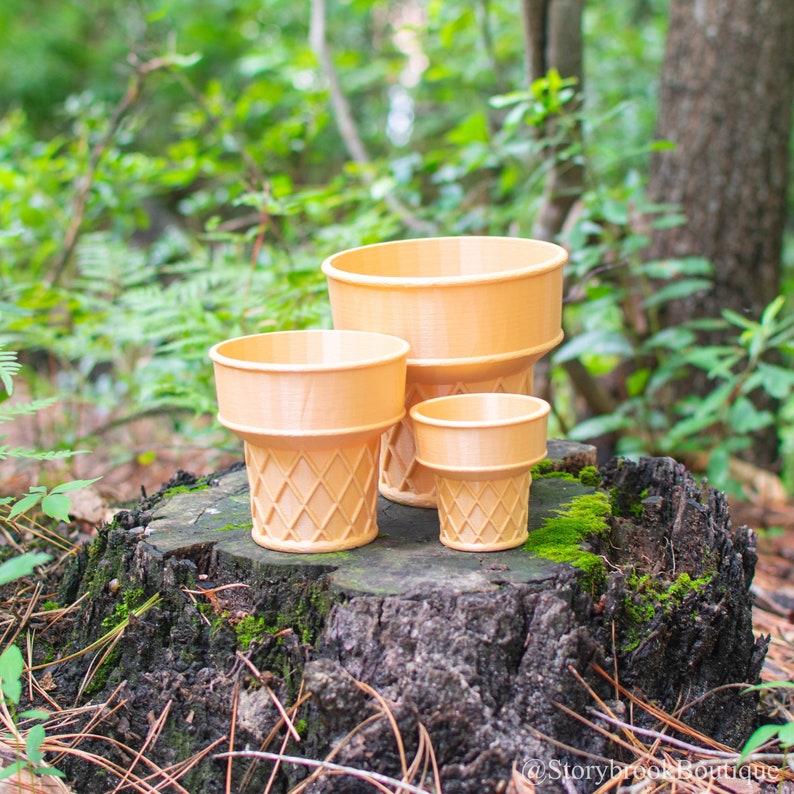 Three 3D printed ice cream cone planters arranged on a moss covered stump in a wooded area. They are made of a light brown plastic and are modeled to look like a cake cone. Each has a wide mouth and the bottom half has a waffle like pattern.