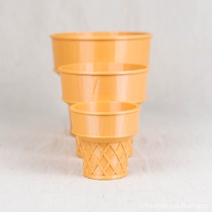 Three ice cream cone planters on a plain, off white studio background. The planters are arranged directly in front of each other with the large in the back, the medium in the middle, and the small in front.