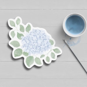 May include: A watercolor illustration of a blue hydrangea flower with green leaves. The flower is surrounded by a white border.