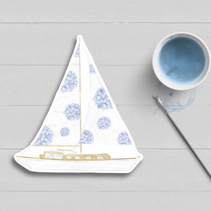 May include: A white sailboat with a blue and white floral pattern. The sailboat is on a white wooden background.