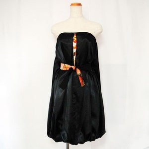May include: A black strapless dress with a fitted bodice and a gathered skirt. The dress has a colorful patterned ribbon tied at the waist.