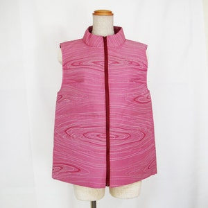 May include: A sleeveless pink vest with a white and pink swirl pattern and a red zip down the front.
