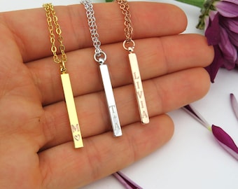 May include: Three gold bar necklaces with personalized engravings. The necklaces are on a hand, with the bar pendants hanging down. The engravings on the bars read "M", "T + A", and "Livia".