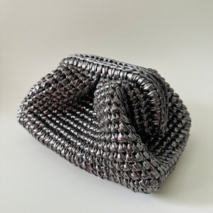 May include: A silver metallic woven clutch bag with a unique, textured design.