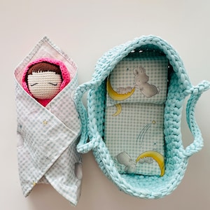 May include: A crocheted baby doll wrapped in a blue and white gingham blanket with stars and moons. The doll is in a blue crocheted basket with a blue and white gingham lining with a moon and bunny rabbit design.