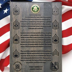 May include: A wooden plaque with a gray background and a black inscription. The inscription is a quote from a First Sergeant in the United States Army. The plaque features a gold coin with a green center and a black and white image of a military insignia. The plaque also features a black and white image of a military rank insignia. The text on the plaque reads: "I swear to perform professional duty... Competence is my watch-word... Officers of my wait will have maximum time to accomplish each duty... I will not fail to accomplish mine... I will earn their respect and confidence as well as that of my Soldiers... I will be loyal to those with whom I serve, superiors, peers, and subordinates alike... I will exercise initiative by taking appropriate action in the absence of orders... I will not compromise my integrity, by my moral courage... I will not forget, nor will I allow my comrades to forget that we are professionals, noncommissioned officers, leaders!" The plaque also features the text "First Sergeant James Harper" and two black and white images of military insignia.