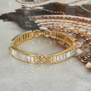 Peut inclure: Un bracelet en or avec un design de chaîne et des cristaux rectangulaires transparents.