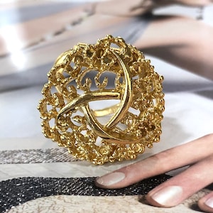 Op de afbeelding: Een gouden ring met een delicaat, ingewikkeld ontwerp. De ring is gemaakt van een filigraanpatroon dat lijkt op een knoop of een geweven ontwerp.