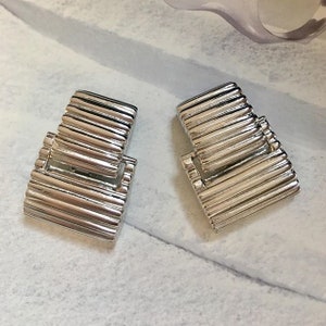 May include: Two silver metal watch band clasps with a ridged design.