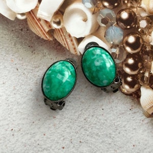 Könnte beinhalten: Ein Paar grüne, ovale Ohrclips mit einer silbernen Metallfassung. Die Ohrringe haben ein marmoriertes Muster.