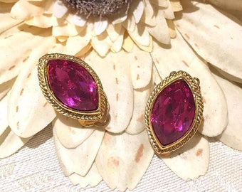 Puede incluir: Un par de pendientes de clip de tono dorado con un gran cristal rosa fucsia facetado en cada pendiente.