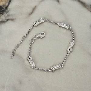 Puede incluir: Una pulsera de cadena en tono plateado con cinco eslabones rectangulares espaciados uniformemente, cada uno engastado con tres pequeñas piedras transparentes. La pulsera incluye un cierre de mosquetón y una cadena extensora ajustable.