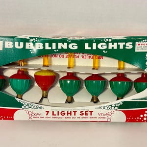 May include: A set of seven bubbling lights in a rectangular cardboard box. The packaging is green, white, and red with the text BUBBLING LIGHTS and 7 LIGHT SET. The lights feature red and green bases with yellow liquid-filled glass tubes.