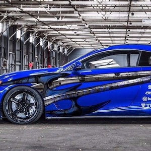 Könnte beinhalten: Ein blauer Sportwagen mit schwarzen und weißen Grafikdesigns an der Seite. Das Auto hat schwarze Räder und einen schwarzen Spoiler. Das Auto hat mehrere Sponsorenlogos an der Seite, darunter Sparco, Cusco, Brembo und TEIN.