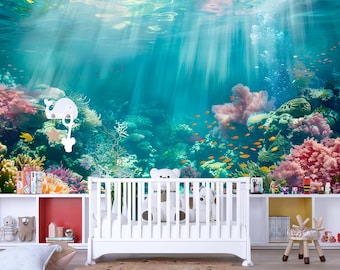 Puede incluir: Una escena de guardería con una cuna blanca y un mural submarino colorido. El mural representa un vibrante arrecife de coral con peces y un móvil de ballena. La habitación tiene estanterías blancas con juguetes y una pequeña silla de madera.