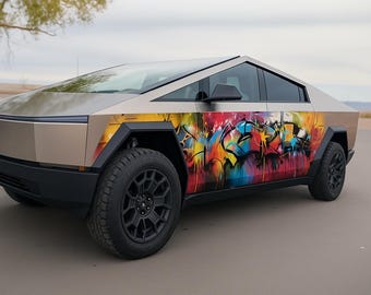 May include: A futuristic, angular, light-colored electric pickup truck with black wheels and tires. The side of the vehicle features vibrant graffiti art in a variety of colors, including red, yellow, blue, and green.