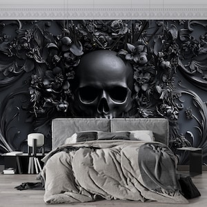 Könnte beinhalten: Ein dunkles, gotisches Schlafzimmer mit einem großen, schwarzen Totenkopf-Wandbild als Kopfteil. Das Wandbild zeigt florale und ornamentale Details. Das Bett hat graue Bettwäsche und einen Nachttisch mit Lampe und Büchern.