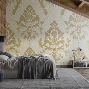 May include: Bedroom interior with a bed, side table, and a patterned wallpaper. The wallpaper features a gold damask design on a cream background. A gray bedspread and rug complement the room's neutral color palette. A black lamp and a wooden wall add contrast.