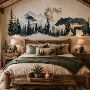 May include: A bedroom featuring a large wall decal of a mountain range, pine forest, full moon, and a bear silhouette. The room includes a wooden bed frame, a green throw blanket, two nightstands with lamps, and a fireplace with stone accents.