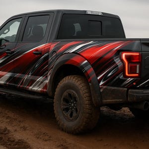 May include: Black Ford Raptor pickup truck with a red, white, and black graphic design on the side. The truck has large off-road tires and is parked on a muddy surface. The taillights are illuminated.