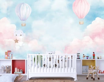 Könnte beinhalten: Eine Szene im Kinderzimmer mit einem weißen Kinderbett, Regalen und dekorativen Gegenständen. Der Hintergrund zeigt einen Himmel mit rosa und blauen Wolken und zwei Heißluftballons. Ein skurriles und farbenfrohes Design für ein Kinderzimmer.