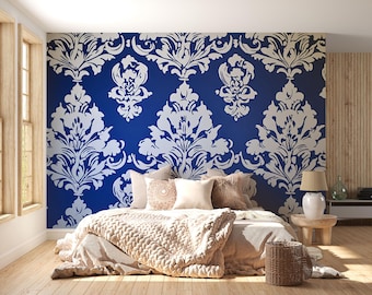 May include: A bedroom with a blue accent wall featuring a white damask pattern. The bed is made with neutral-toned bedding and decorative pillows. A woven basket and a wooden side table with a lamp complete the cozy, inviting space.