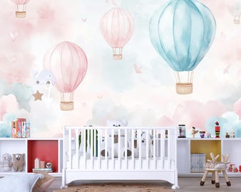 Könnte beinhalten: Ein Kinderzimmer mit einem weißen Kinderbett, Regalen und einem Teppich. Die Tapete zeigt Aquarell-Heißluftballons in Rosa und Blau vor einem pastellfarbenen Himmel mit Wolken. Dekorative Elemente sind Stofftiere und Spielzeug.
