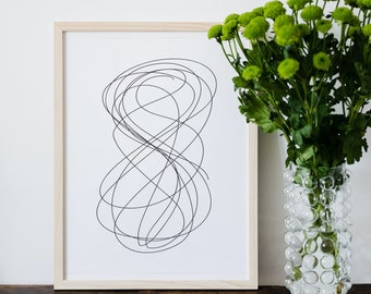 May include: A framed black and white line drawing of a swirling abstract design. The frame is light wood and the drawing is on a white background. A vase of green flowers is to the right of the frame.
