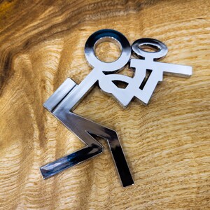May include: A silver metal sculpture of a person holding a smaller person. The sculpture is on a wooden surface.