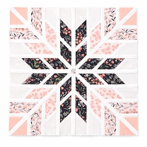 Puede incluir: Un bloque de edredón cuadrado con un diseño de estrella. El bloque de edredón está compuesto de tela con estampado floral blanco, rosa claro y negro. La estrella está delineada con tiras blancas. Los estampados florales incluyen flores rosas y hojas verdes.