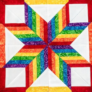 May include: A colorful quilt block featuring a starburst design. The star is composed of rainbow-colored fabric strips radiating from the center, with white and red accents. The quilt block is square and has a vibrant, eye-catching appearance.
