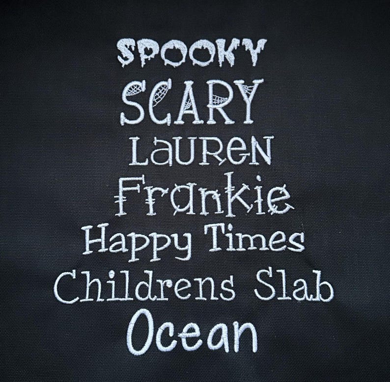 May include: A black fabric tote bag with white embroidered text that reads "Spooky Scary Lauren Frankie Happy Times Childrens Slab Ocean".