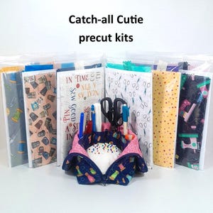 May include: A set of precut fabric kits for making a catch-all cutie sewing project. The kits include a variety of colorful fabrics with sewing-themed patterns, such as sewing machines, spools of thread, and pins. The kits are packaged in clear plastic bags.