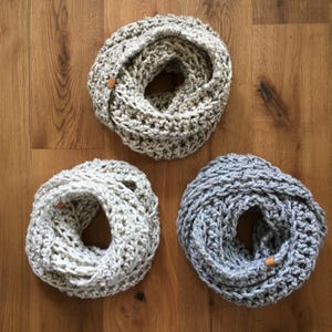 Könnte beinhalten: Drei gehäkelte Infinity-Schals in verschiedenen Farben und Texturen. Die Schals sind aus einem dicken Garn gefertigt und haben ein schlichtes, elegantes Design. Die Schals sind eine großartige Möglichkeit, jedem Outfit einen Hauch von Wärme und Stil zu verleihen.