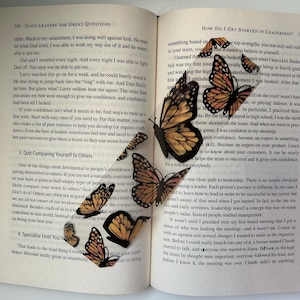 May include: A book with a bookmark featuring a collage of orange and black butterflies. The book is open to a page with the title "How Do I Get Started in Leadership?" and text about leadership.