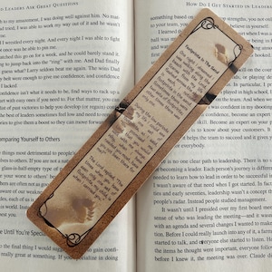 May include: A rectangular bookmark with a brown border and text from the poem "Footprints in the Sand." The bookmark features a light brown background with a printed image of footprints. The bookmark is placed on top of an open book.