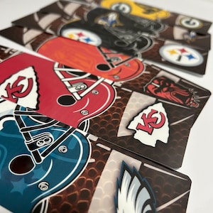 May include: A collection of rectangular cards featuring various American football team logos and helmet designs. The cards display logos for teams like the Kansas City Chiefs, Cleveland Browns, and Philadelphia Eagles, set against a football-themed background.
