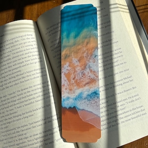 Puede incluir: Primer plano de una escena de playa con agua azul turquesa rompiendo sobre una costa arenosa. El agua es clara y la arena es de color marrón claro. La imagen está tomada desde un ángulo alto, ofreciendo una vista de pájaro de la playa.